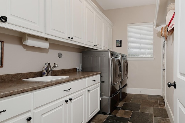 laundry room featuring baseboards, washer and clothes dryer, stone tile flooring, cabinet space, and a sink