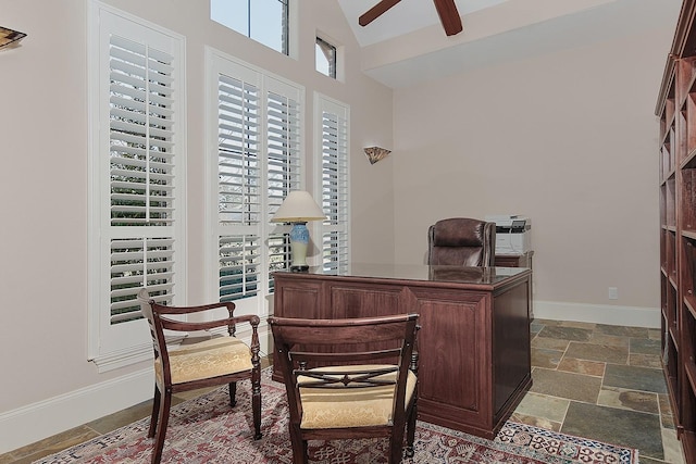 home office with ceiling fan, baseboards, high vaulted ceiling, and stone tile flooring