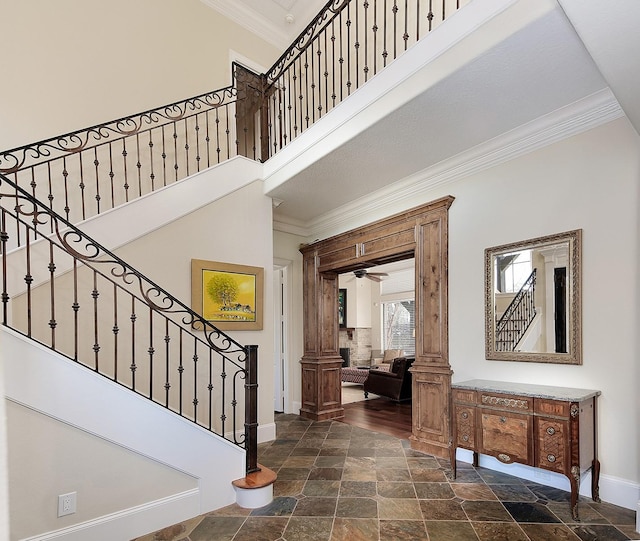 stairs with ornamental molding, stone tile flooring, a high ceiling, decorative columns, and baseboards