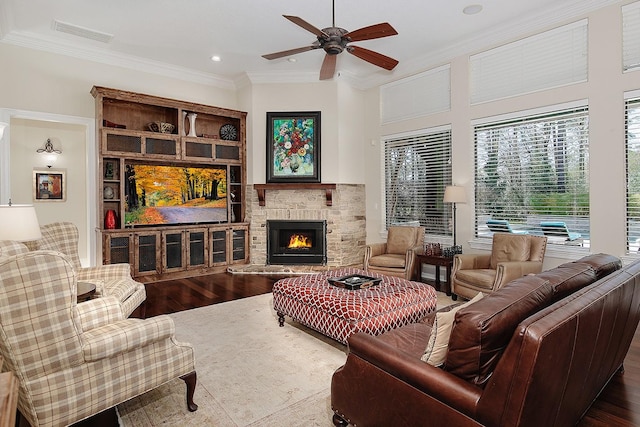 living area with visible vents, crown molding, a fireplace, wood finished floors, and a ceiling fan