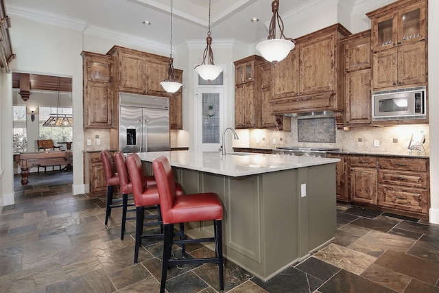 kitchen featuring stone tile flooring, built in appliances, tasteful backsplash, and a sink