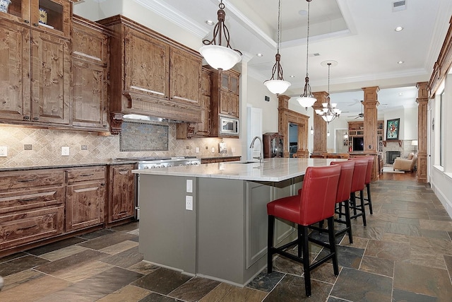 kitchen featuring crown molding, stone tile floors, stainless steel appliances, a raised ceiling, and a sink