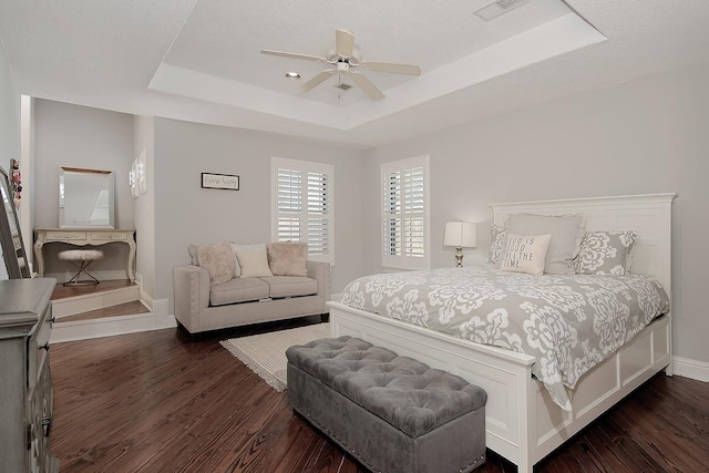 bedroom with visible vents, baseboards, a tray ceiling, and dark wood-style flooring