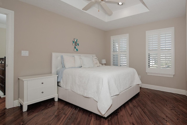 bedroom with a raised ceiling, dark wood-style floors, baseboards, and ceiling fan