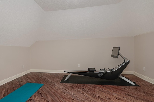 workout area featuring lofted ceiling, wood finished floors, baseboards, and a textured ceiling