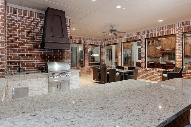 kitchen with light stone counters, a ceiling fan, brick wall, recessed lighting, and custom range hood