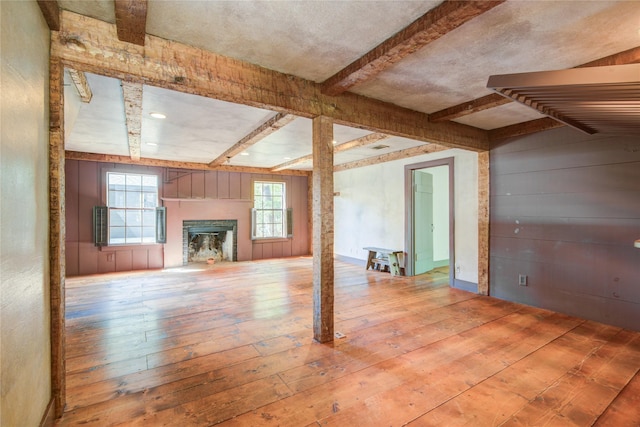 unfurnished living room featuring a wealth of natural light, hardwood / wood-style floors, a glass covered fireplace, and beam ceiling