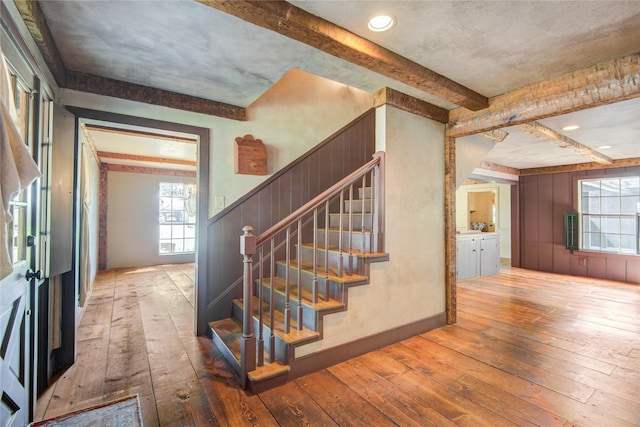 staircase featuring wood walls, wood-type flooring, and beam ceiling