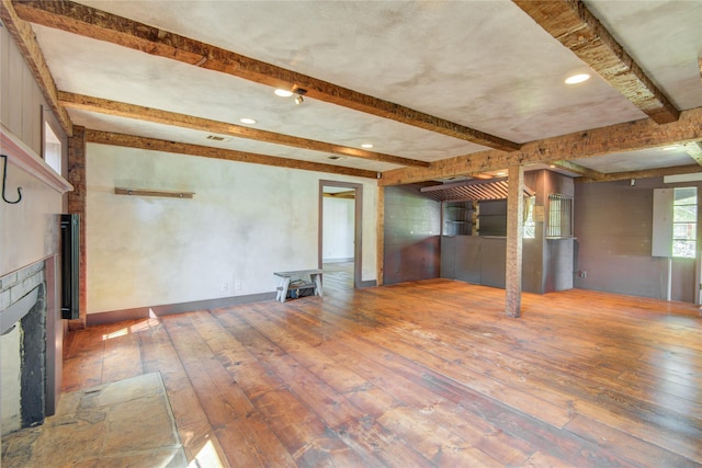 unfurnished living room featuring a tile fireplace, wood-type flooring, visible vents, and beam ceiling