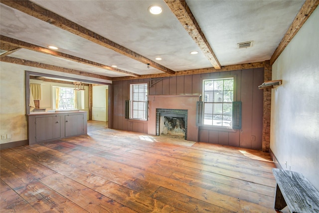 unfurnished living room featuring visible vents, hardwood / wood-style floors, beamed ceiling, wood walls, and a fireplace