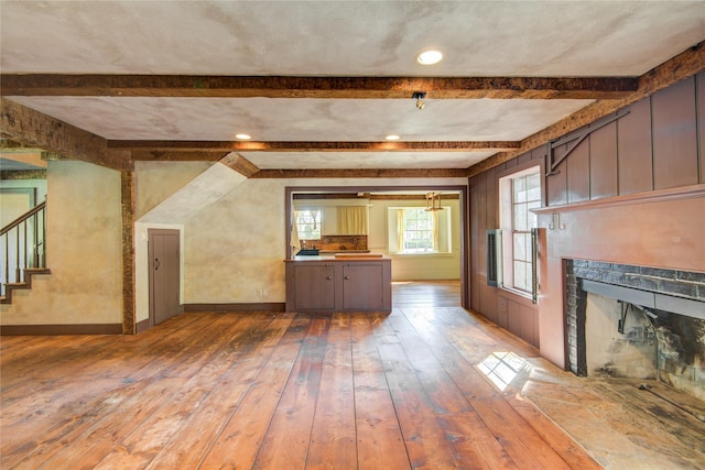 unfurnished living room featuring hardwood / wood-style flooring, a fireplace, beamed ceiling, baseboards, and stairs