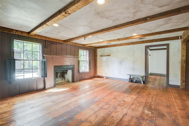 unfurnished living room with a fireplace, visible vents, hardwood / wood-style floors, and beamed ceiling