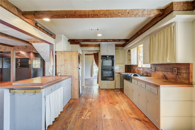 kitchen featuring beam ceiling, dobule oven black, visible vents, a sink, and light wood-type flooring