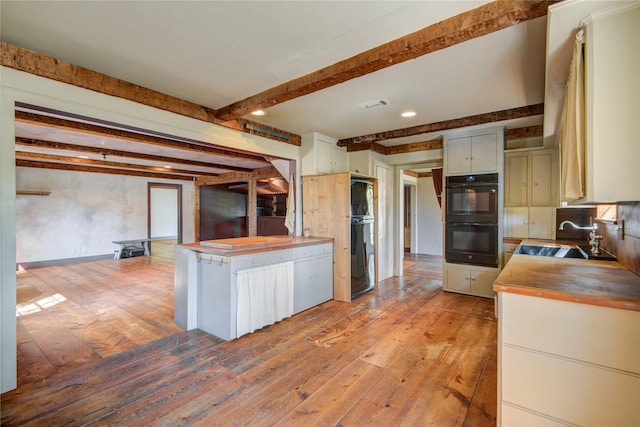 kitchen with dobule oven black, butcher block counters, visible vents, and a sink