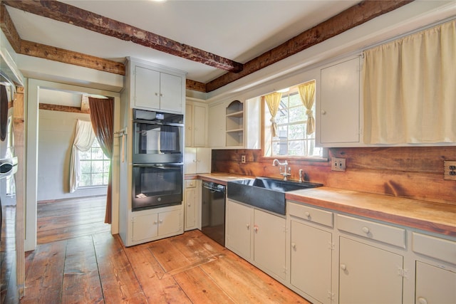 kitchen featuring light wood-style floors, butcher block countertops, beamed ceiling, black appliances, and a sink