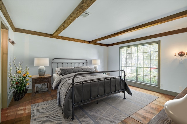 bedroom with baseboards, beamed ceiling, wood-type flooring, and visible vents