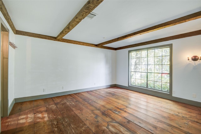 spare room featuring wood-type flooring, visible vents, baseboards, and beam ceiling