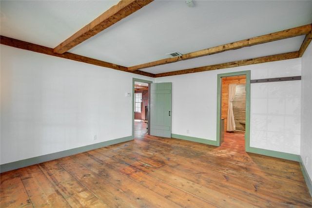 spare room featuring wood-type flooring, visible vents, beamed ceiling, and baseboards