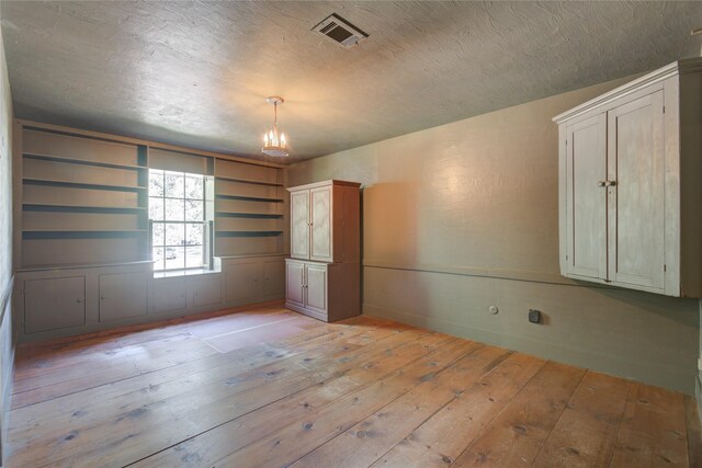 unfurnished room featuring visible vents, a notable chandelier, a textured ceiling, and light wood-style flooring