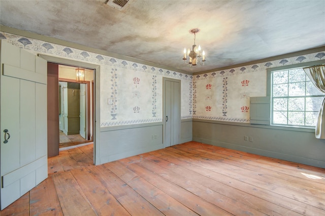 unfurnished room with wallpapered walls, wood-type flooring, visible vents, and an inviting chandelier