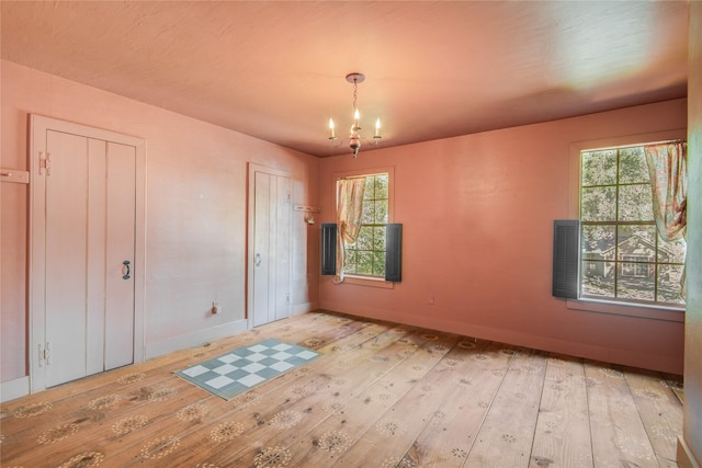 empty room with baseboards, a notable chandelier, wood-type flooring, and plenty of natural light