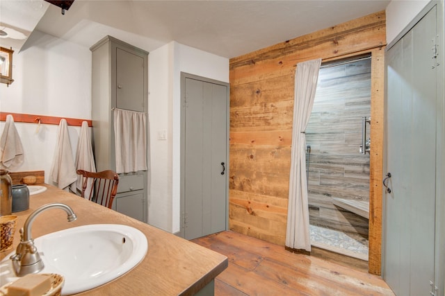 bathroom featuring hardwood / wood-style flooring, wooden walls, double vanity, and a sink