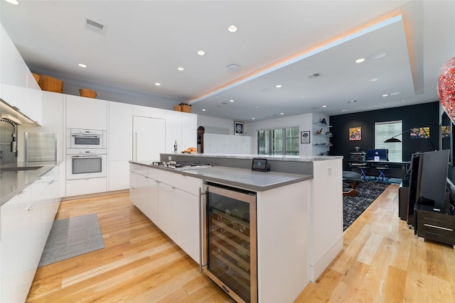 kitchen featuring wine cooler, light wood-style flooring, double oven, white cabinetry, and modern cabinets