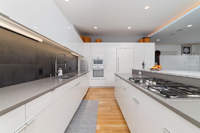 kitchen with stainless steel gas stovetop, backsplash, light wood-style flooring, a sink, and modern cabinets