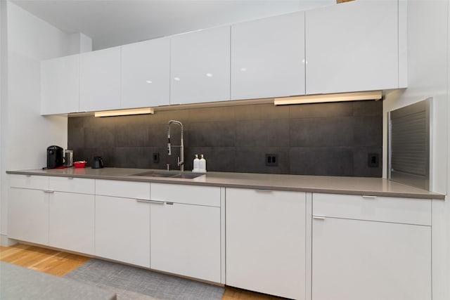 kitchen with white cabinetry, a sink, light wood-style flooring, and decorative backsplash