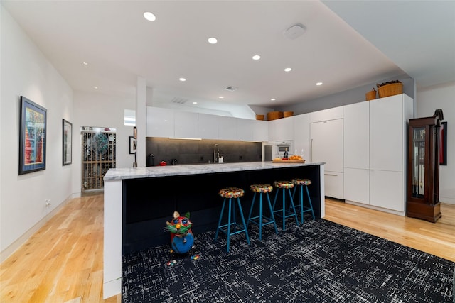 kitchen featuring light wood-type flooring, modern cabinets, decorative backsplash, and white cabinets