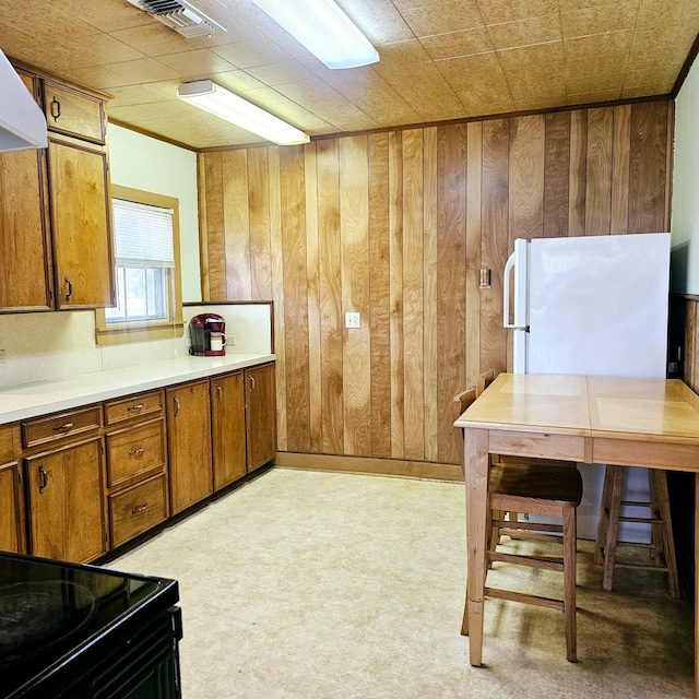 kitchen with brown cabinets, visible vents, black electric range oven, wooden walls, and extractor fan