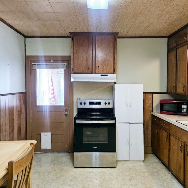 kitchen with electric stove, a wainscoted wall, light countertops, wood walls, and under cabinet range hood