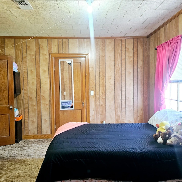 carpeted bedroom with ornamental molding, visible vents, and wood walls