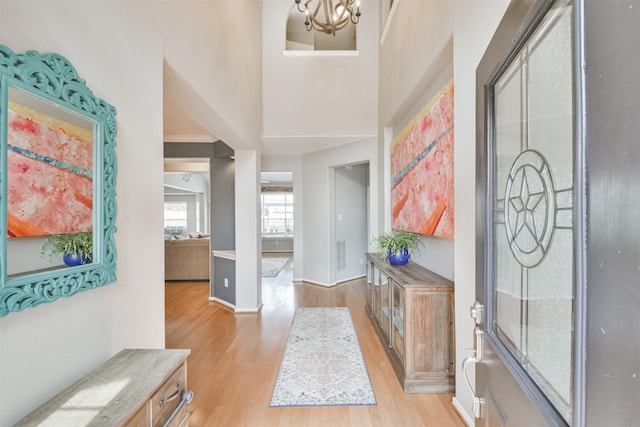 entrance foyer featuring visible vents, baseboards, a towering ceiling, light wood-style flooring, and a notable chandelier