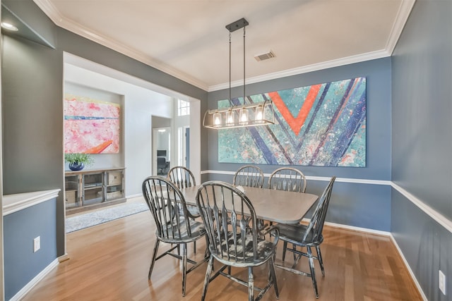 dining room featuring ornamental molding, wood finished floors, visible vents, and baseboards