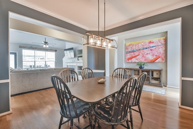 dining room with baseboards, wood finished floors, crown molding, a fireplace, and ceiling fan with notable chandelier