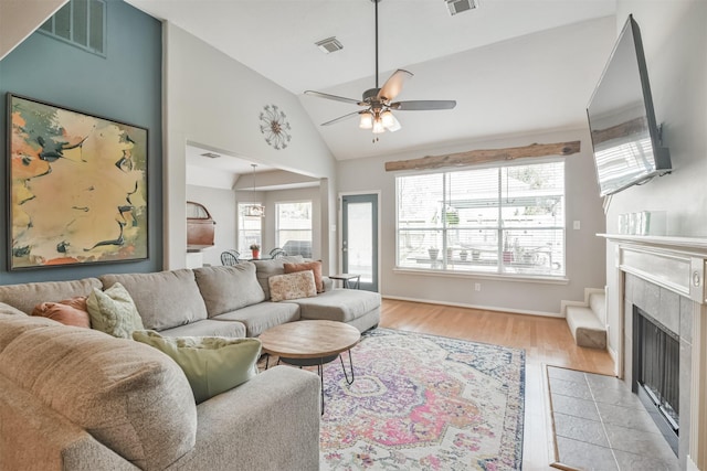 living area featuring light wood-style floors, ceiling fan, visible vents, and a tile fireplace