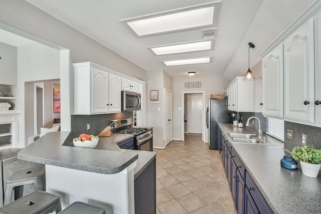 kitchen with appliances with stainless steel finishes, a peninsula, a kitchen bar, white cabinetry, and a sink