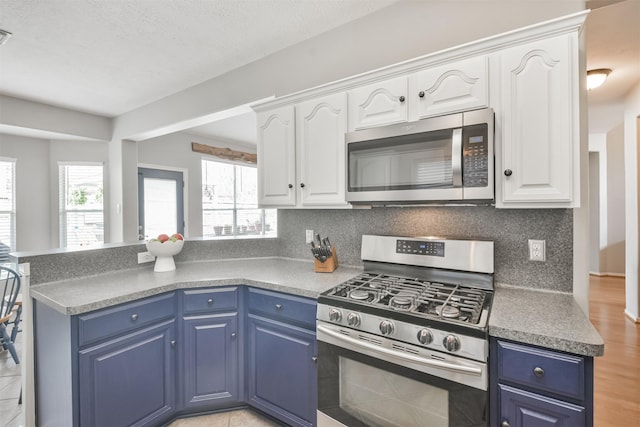 kitchen featuring tasteful backsplash, appliances with stainless steel finishes, white cabinetry, blue cabinets, and a peninsula