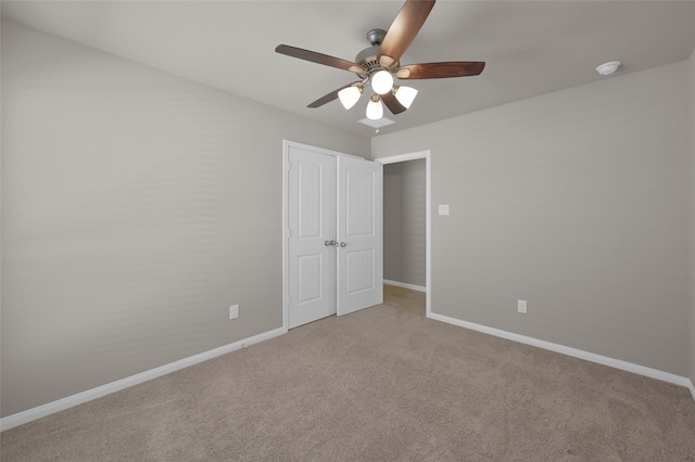 unfurnished bedroom featuring light carpet, ceiling fan, baseboards, and a closet