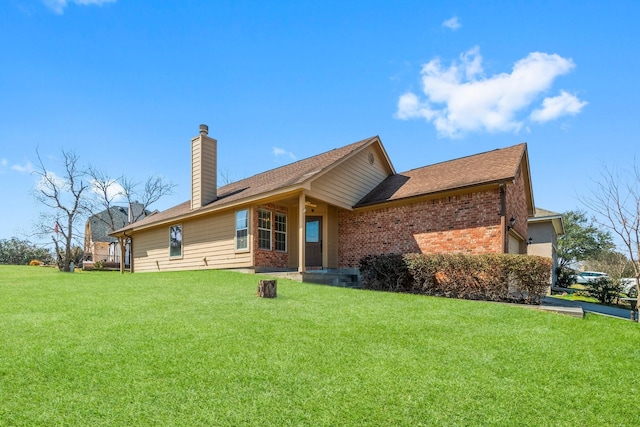 rear view of house with a yard, a chimney, and brick siding