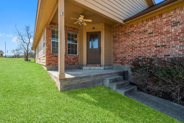 view of exterior entry featuring brick siding, a ceiling fan, and a yard