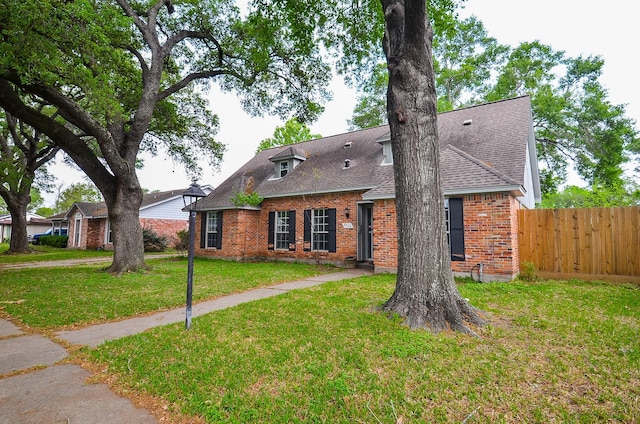 view of front of property with a front yard, fence, brick siding, and roof with shingles