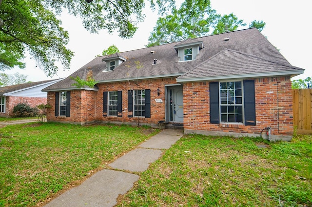 view of front of home with brick siding, fence, roof with shingles, and a front lawn