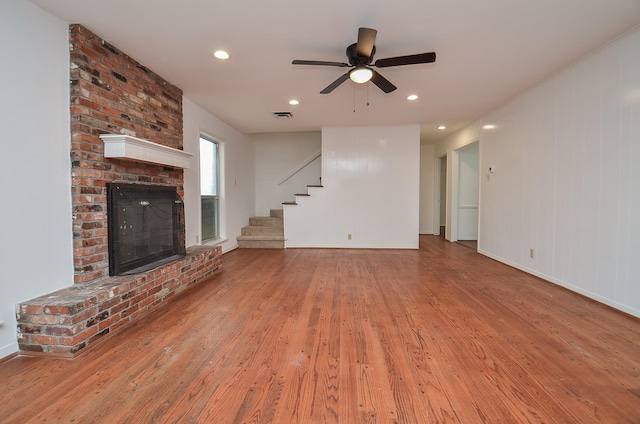 unfurnished living room with visible vents, wood finished floors, stairway, and a brick fireplace