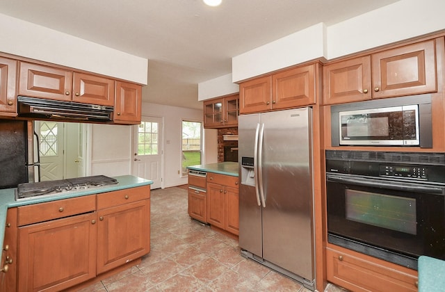 kitchen with brown cabinetry, appliances with stainless steel finishes, under cabinet range hood, and glass insert cabinets