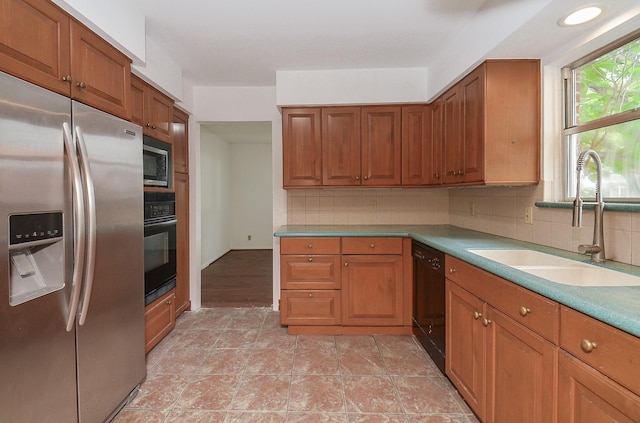 kitchen with light countertops, backsplash, a sink, black appliances, and brown cabinets