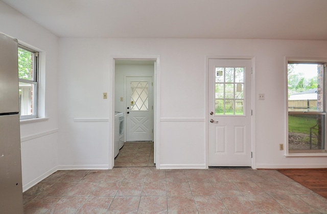 entrance foyer featuring light tile patterned floors, washer / dryer, a healthy amount of sunlight, and baseboards