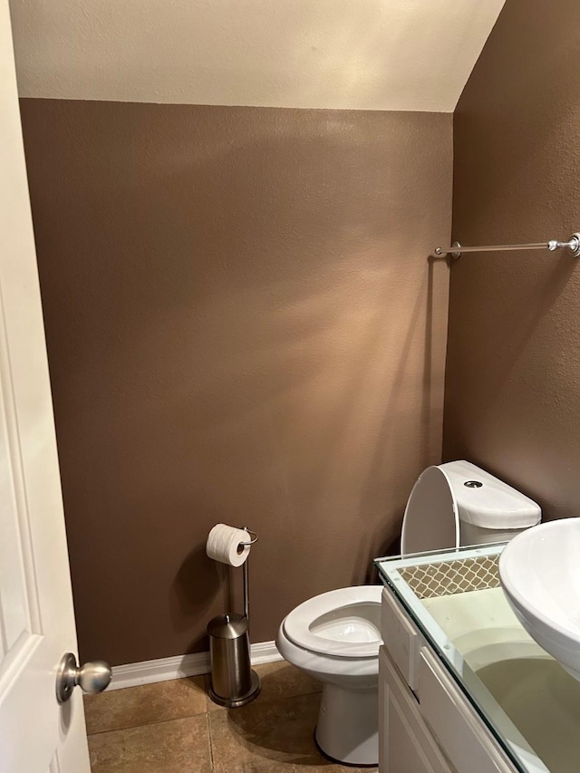 half bathroom with tile patterned flooring, baseboards, vanity, and toilet