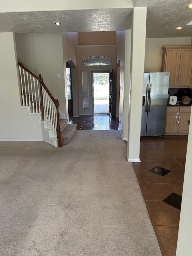 entrance foyer featuring dark tile patterned floors, arched walkways, dark colored carpet, and a textured ceiling